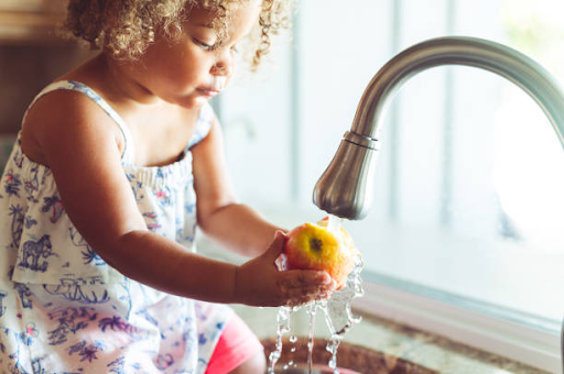 A child washes an apple under a modern, water-efficient faucet, symbolizing sustainability at Binghatti Hills.